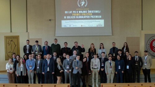 Organizatorzy i prelegenci pozują do wspólnego zdjęcia na tle plakatu konferencji.